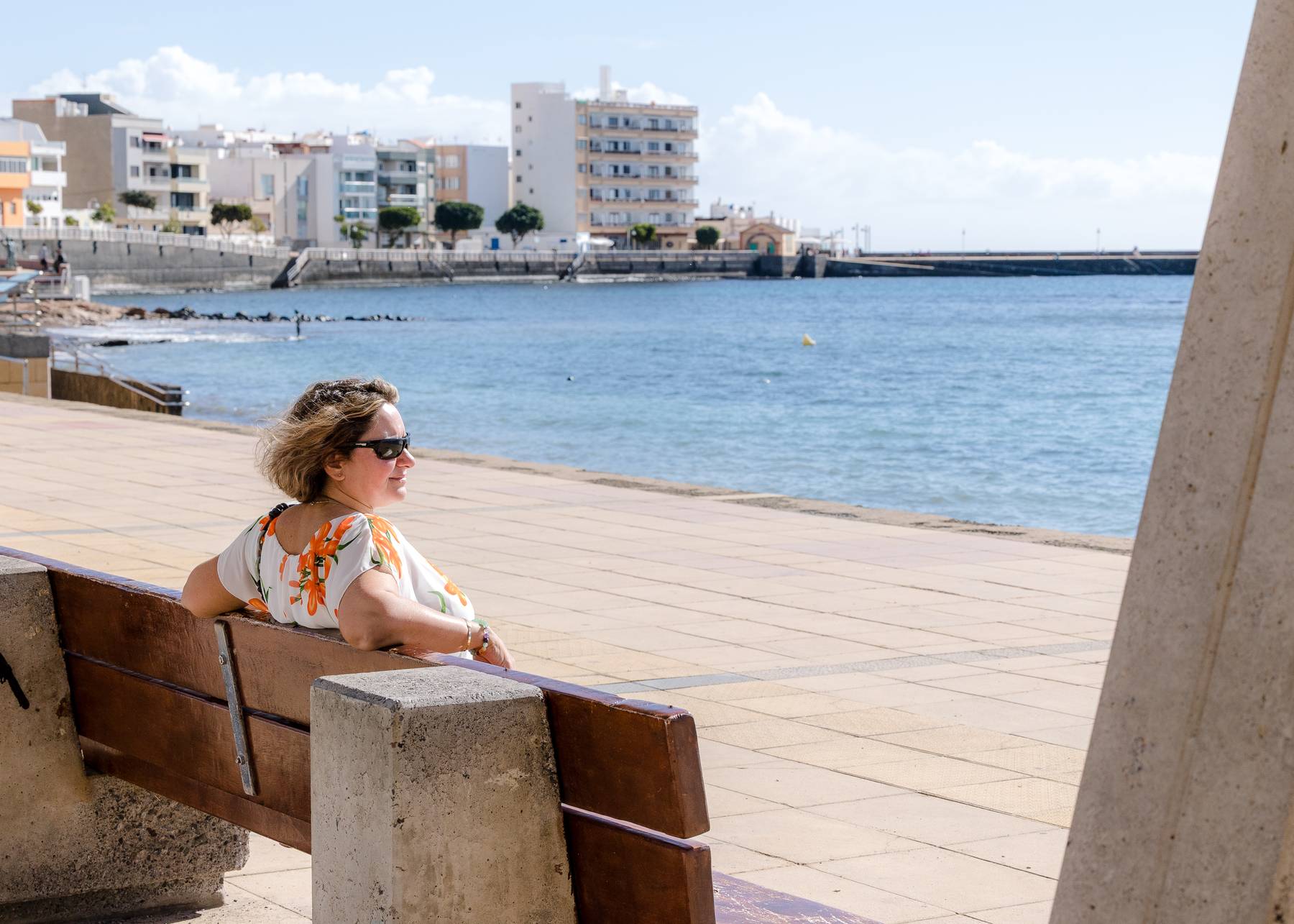Sian sitting on a bench by the sea, looking out to the distance